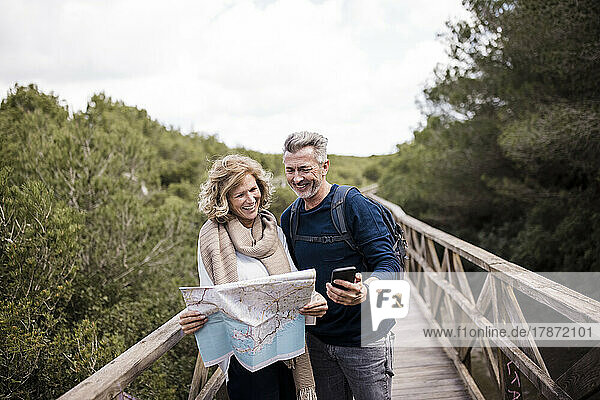 Smiling mature couple holding map standing on footbridge