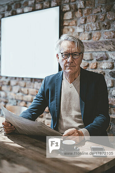 Confident senior businessman with newspaper in cafe
