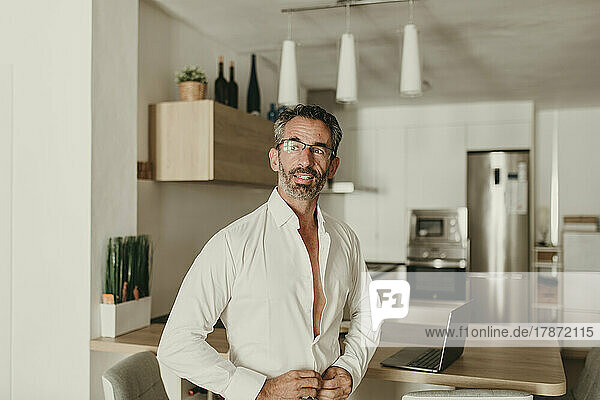 Businessman buttoning shirt in kitchen at home