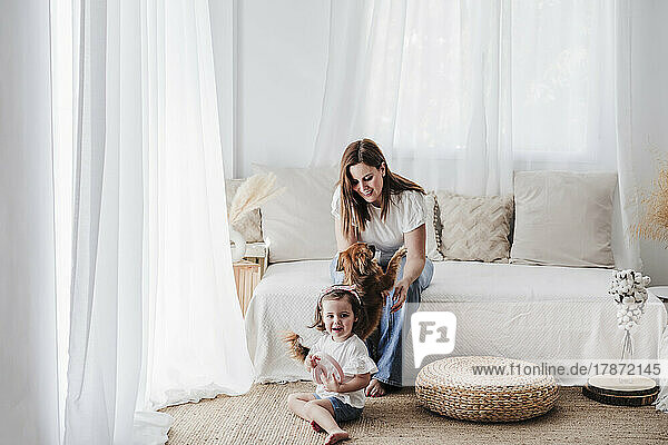 Happy mother and daughter playing with dog in living room at home