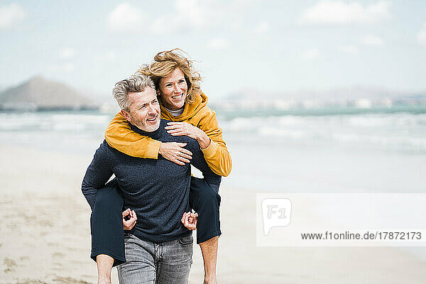 Happy man giving piggyback ride to woman on shore at beach