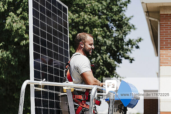 Smiling electrician with solar panel standing in hydraulic platform