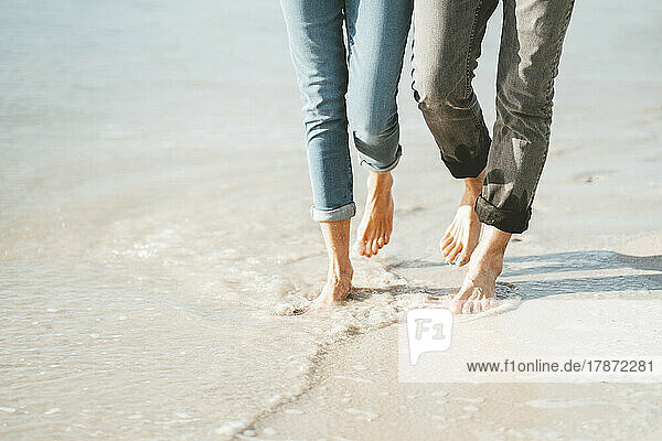 Mature couple walking barefoot on shore at beach