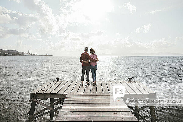 Mature couple standing on jetty under cloudy sky