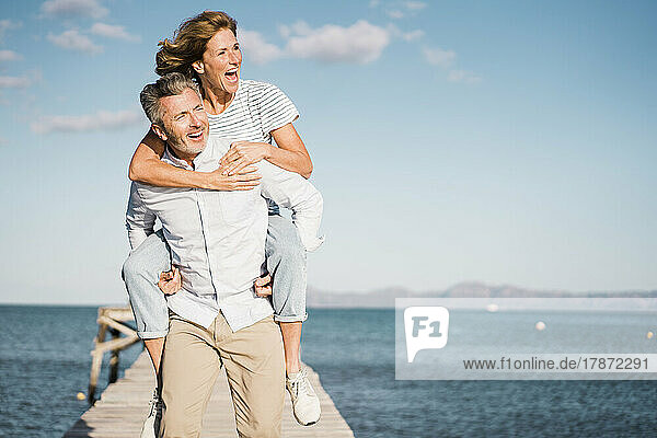 Cheerful man giving piggyback ride to woman on jetty