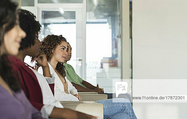 Young businesswoman sitting amidst colleagues in office