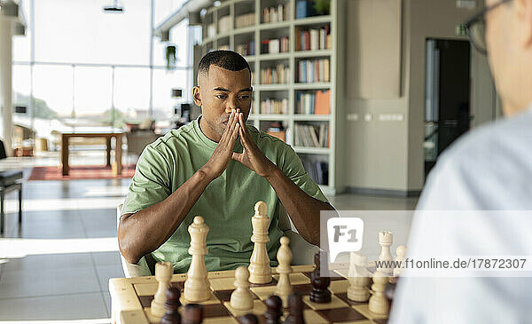 Serious businessman hands clasped looking at chess board in office