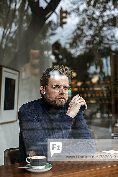 Thoughtful mature businessman in cafe seen through glass window