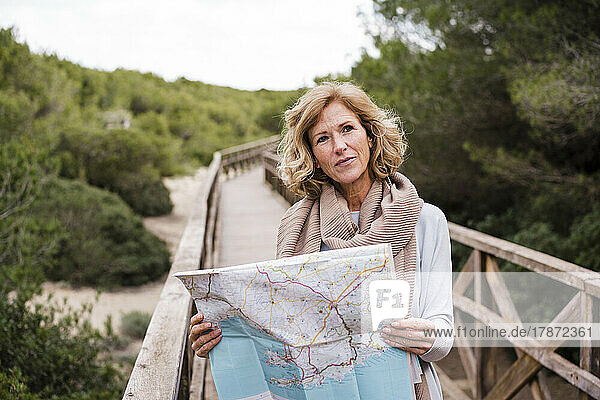 Smiling mature woman with map standing on footbridge