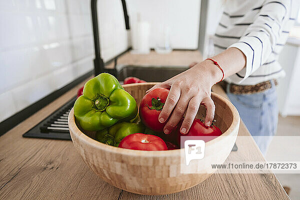 Woman picking up tomato from bowl for washing in kitchen