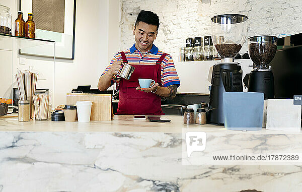 Smiling young man with coffee mug and cup working in cafe