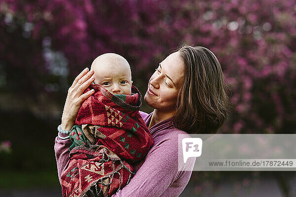 Smiling mother carrying baby boy wrapped in blanket at garden