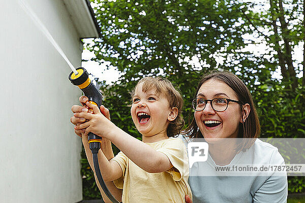 Playful mother and son spraying water through garden hose