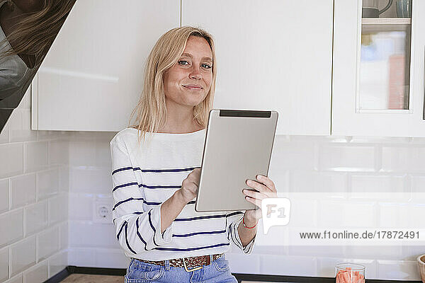 Smiling woman holding tablet PC in kitchen at home