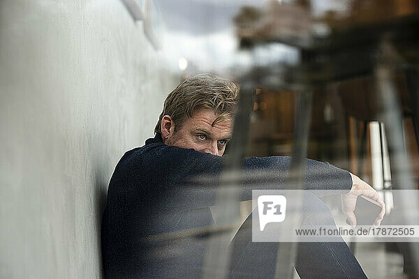 Stressed businessman sitting in cafe seen through glass window