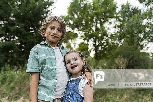 Smiling brother and sister standing at park