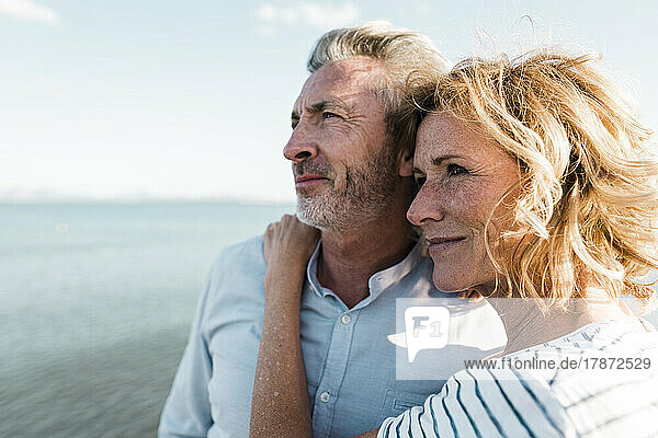 Smiling blond woman with man standing at beach on sunny day