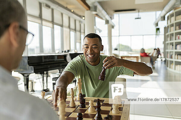 Glücklicher Geschäftsmann  der mit einem Kollegen im Büro eine Schachfigur in die Hand nimmt und ein Brettspiel spielt