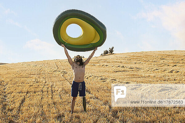 Shirtless man with prosthetic leg carrying inflatable ring at field on sunny day