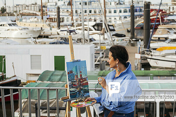 Woman painting on easel at harbor