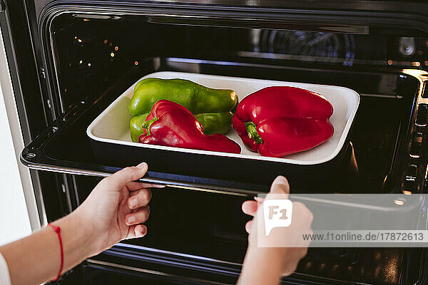 Woman putting bell peppers in oven at home