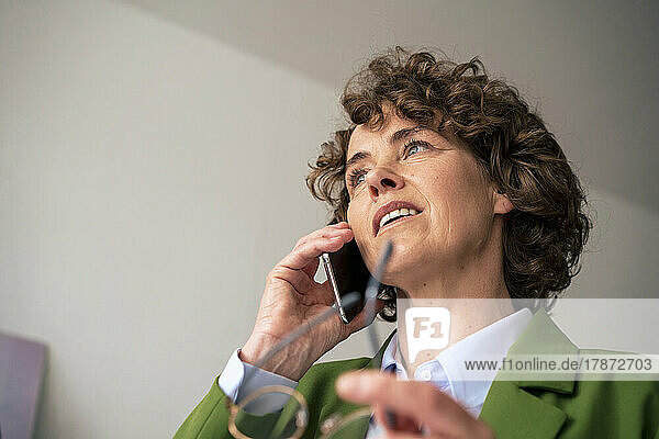 Reife Geschäftsfrau mit lockigem Haar  die auf dem Smartphone spricht