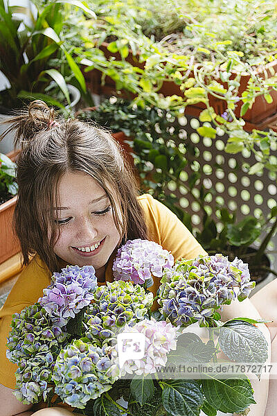 Smiling teenage girl looking at hydrangea flowers on balcony