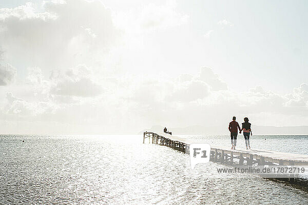 Älteres Paar hält sich an den Händen und geht auf dem Steg über dem Meer