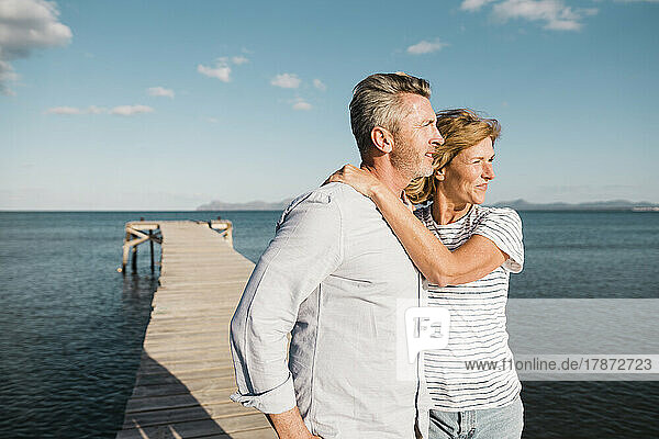 Smiling woman with man standing at jetty in front of sea