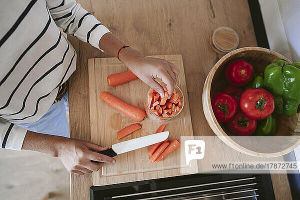 Woman putting slices of carrots in jar at home