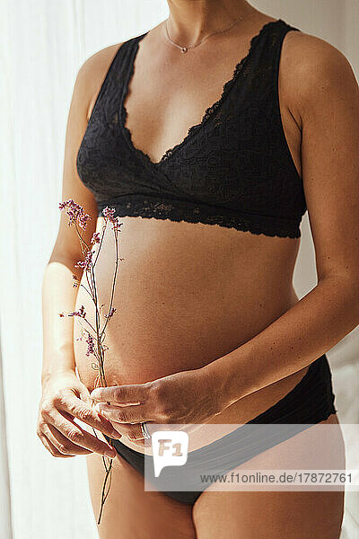 Pregnant woman holding dry flowers at home