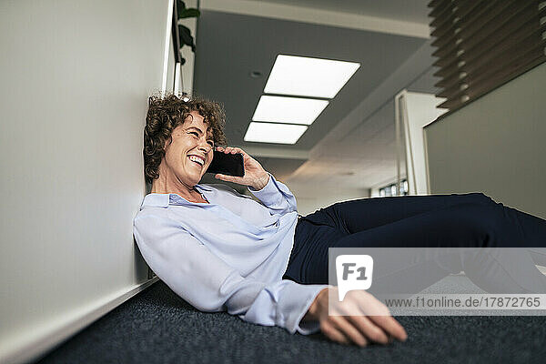 Fröhliche Geschäftsfrau  die im Büro auf dem Smartphone spricht