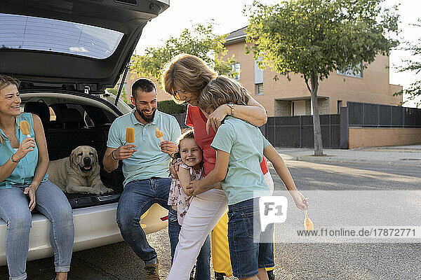Siblings embracing grandmother by parents sitting with dog in car trunk