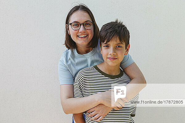 Smiling mother embracing son in front of white wall