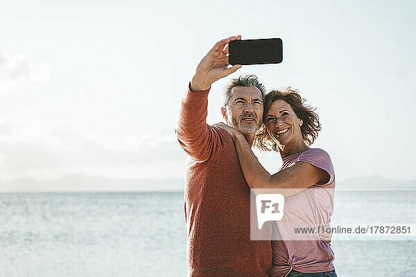 Happy couple taking selfie through smart phone in front of sea
