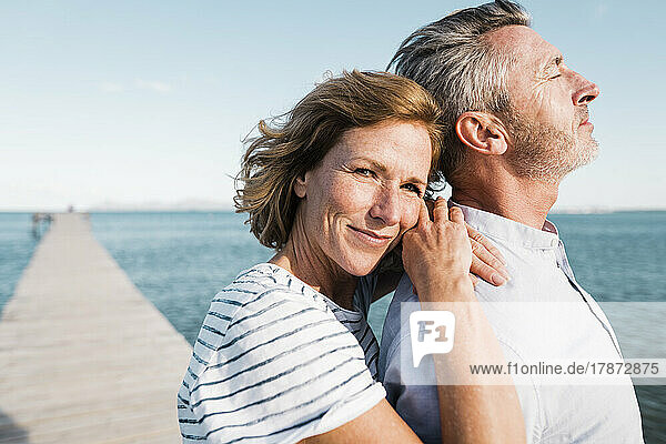 Smiling mature woman standing with man at jetty on sunny day