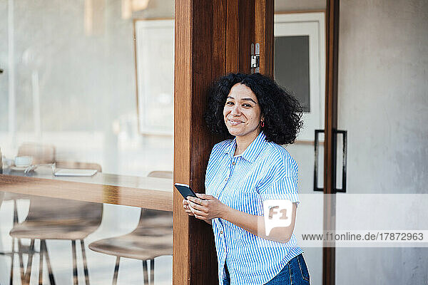 Happy woman with mobile phone leaning on door