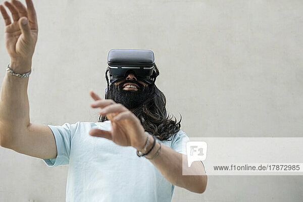 Smiling bearded man wearing virtual reality simulator in front of wall