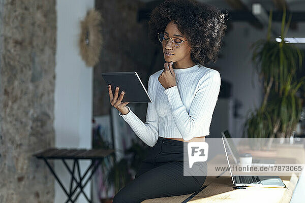 Nachdenkliche Geschäftsfrau blickt im Büro auf den Tablet-PC