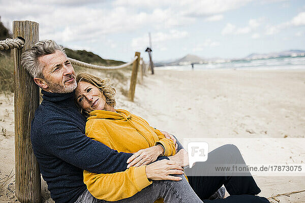 Smiling mature woman with man leaning on pole at beach