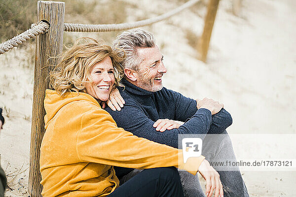 Happy mature woman with man sitting at beach