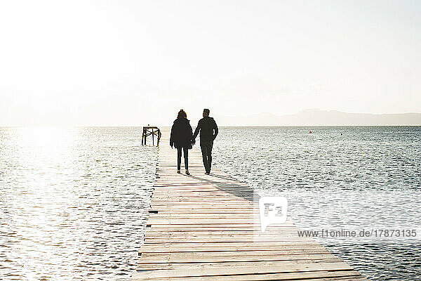 Couple holding hands walking on jetty over sea