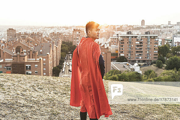Young businessman with red cape standing on top of hill