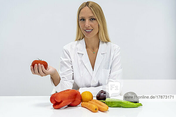 Smiling nutritionist with vegetables sitting at desk in hospital