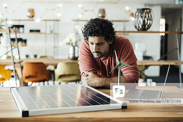Businessman examining solar panel by wind turbine model at office
