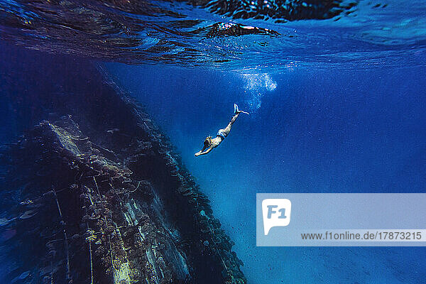 Frau taucht unter Wasser in der Nähe eines Schiffswracks im Meer