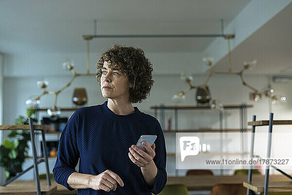 Businesswoman with curly hair holding smart phone in office