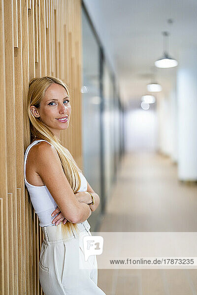 Smiling businesswoman leaning on wall at office