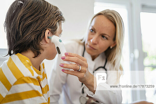 Female doctor examining boy taking his temperature