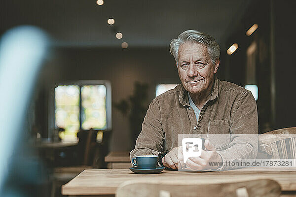 Smiling senior man with mobile phone in cafe